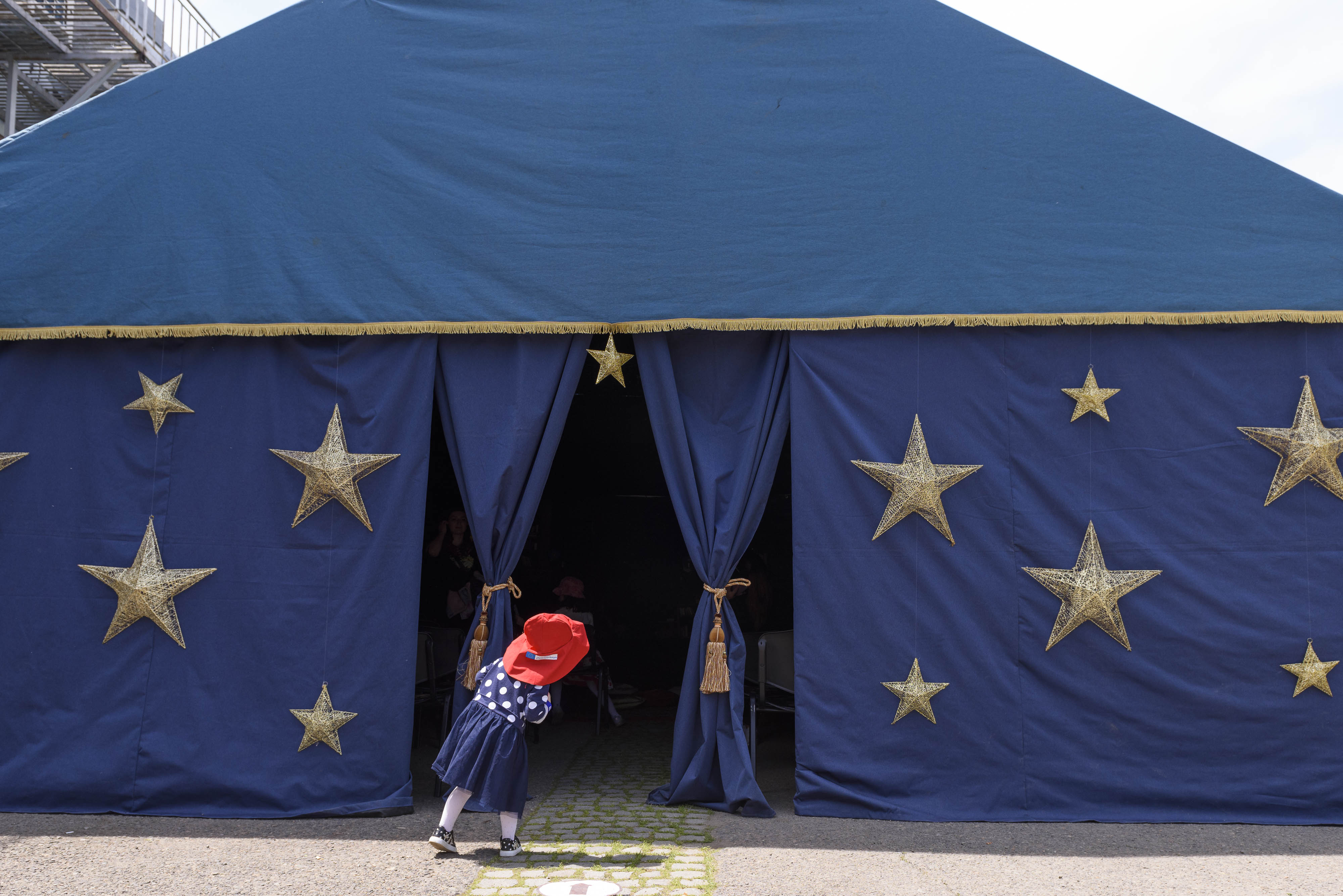 A red-hat baby looking inside a blue magic tent with yellow stars