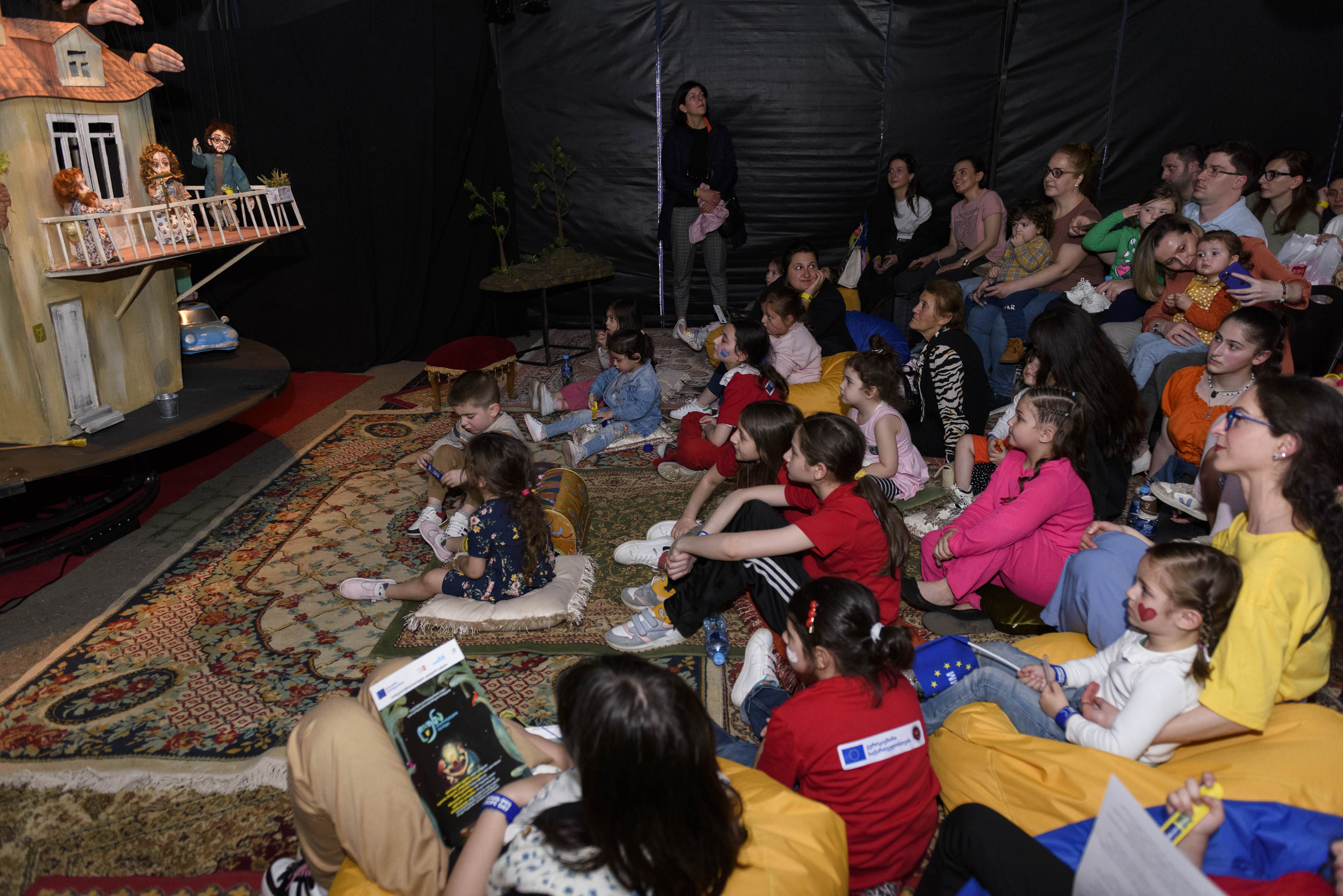 A bunch of children and adults sitting on the carpet watching a puppet show