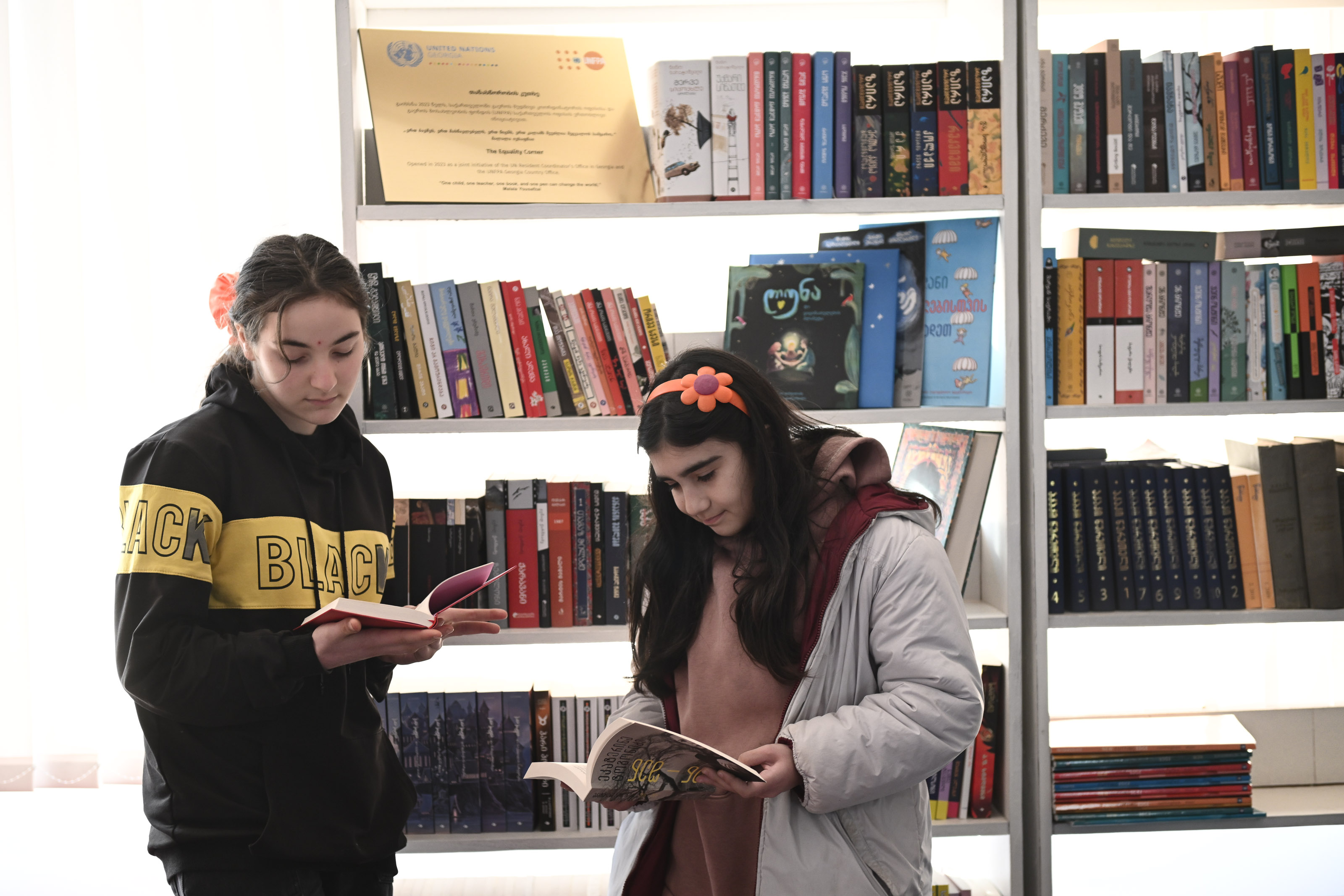 Two adolescent girls holding books, reading