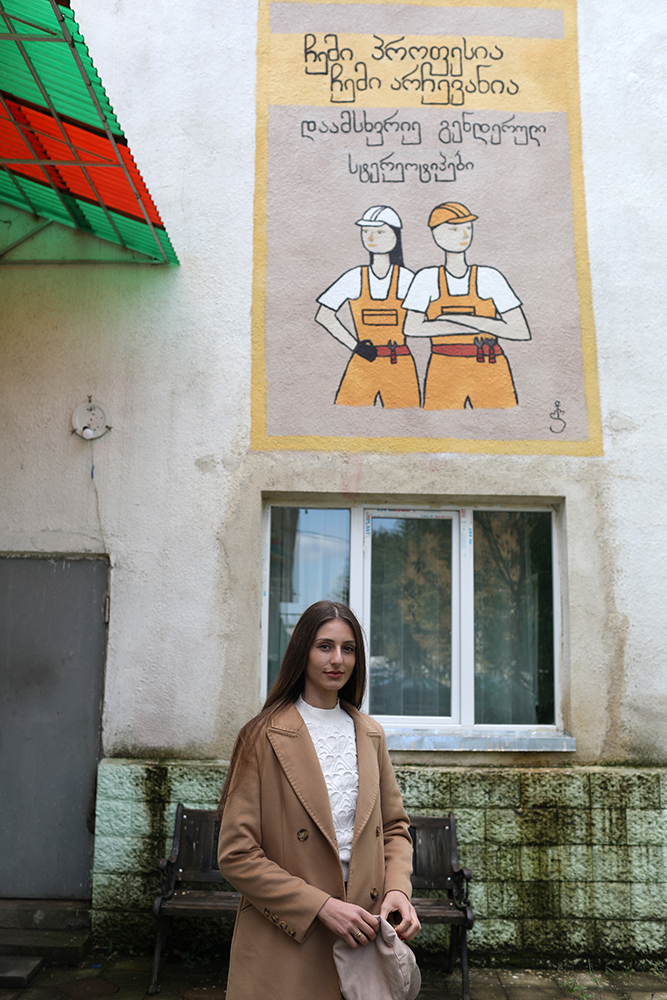 Ana Datiashvili standing in front of her painting at a kindergarten wall