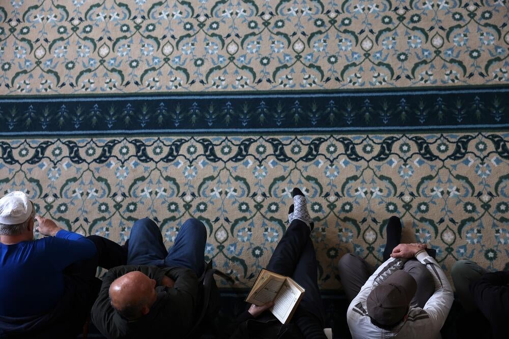 Four Muslim men sitting on a floor. One of them is holding a book which is open