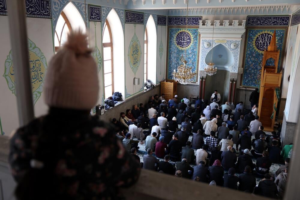 A kid wearing a hat is looking down to men sitting on the floor of a Mosque