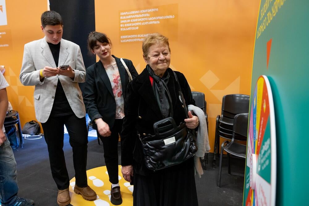 Several people, including an elder woman are standing at the UNFPA orange corner