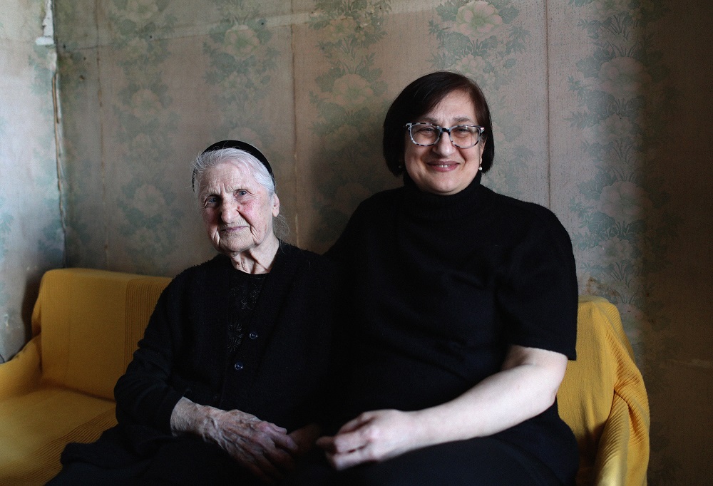 Two women wearing black are sitting together holding with hands