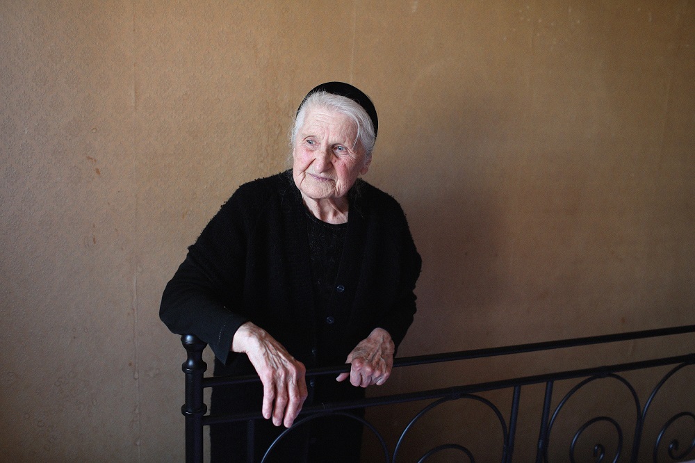 An elder woman wearing black is sitting on a chair