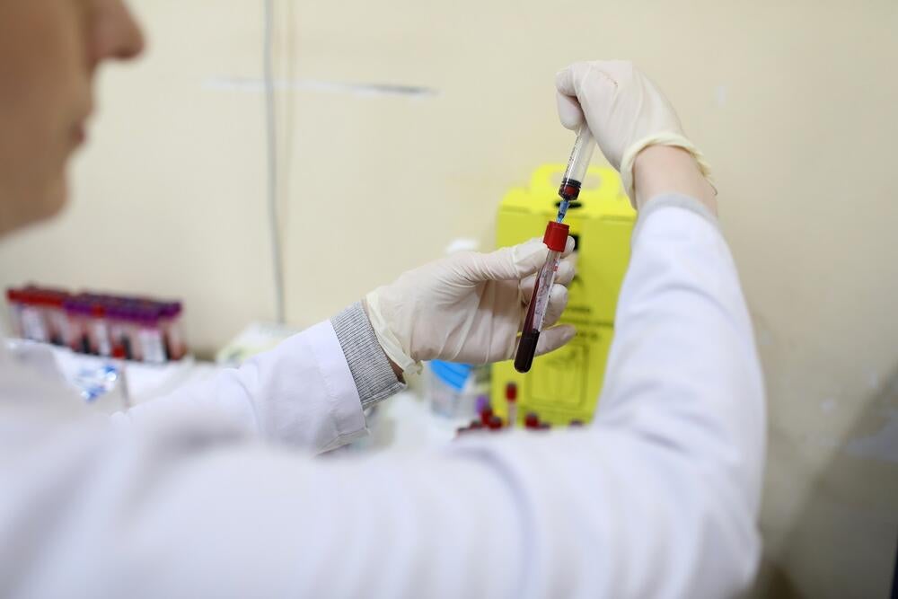 A medical personnel wearing a white collar is placing blood from the syringe to the tester
