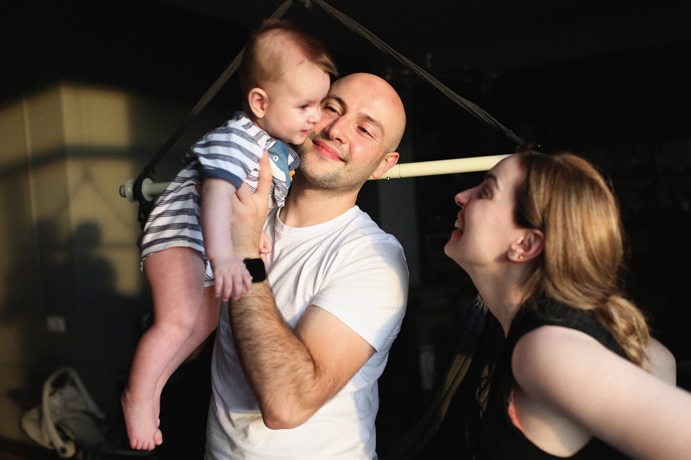 The father holding his baby-boy, while the mother is trying to entertain him