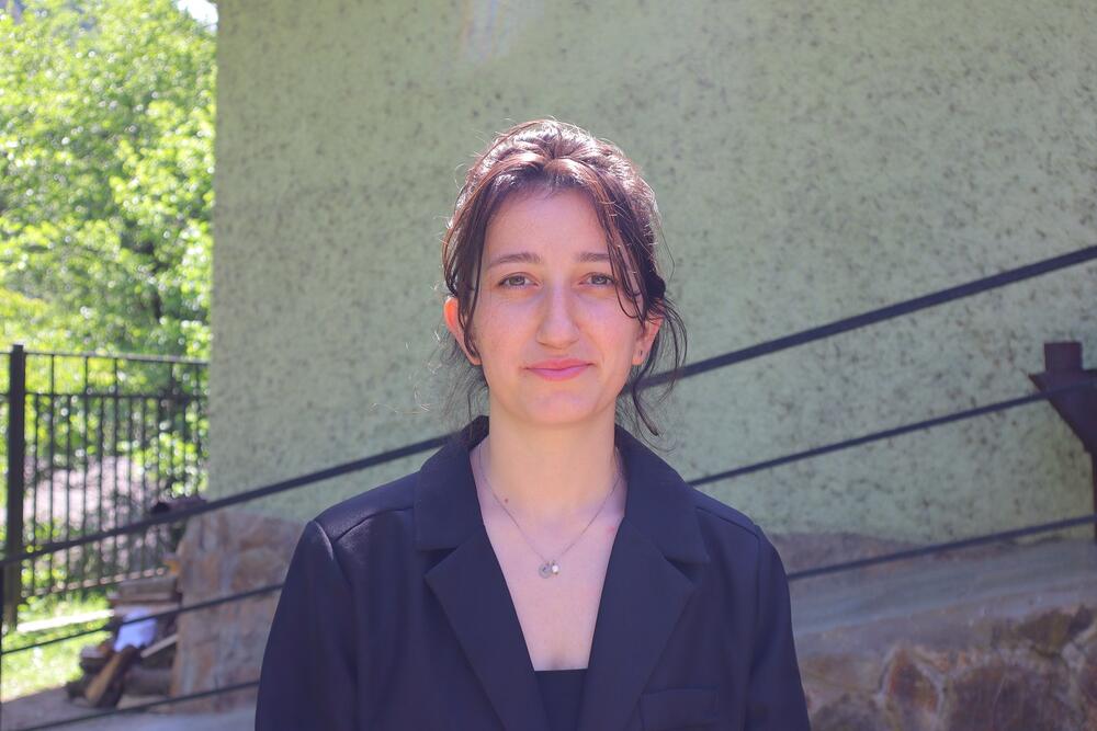 A young woman wearing black suit is standing outdoors