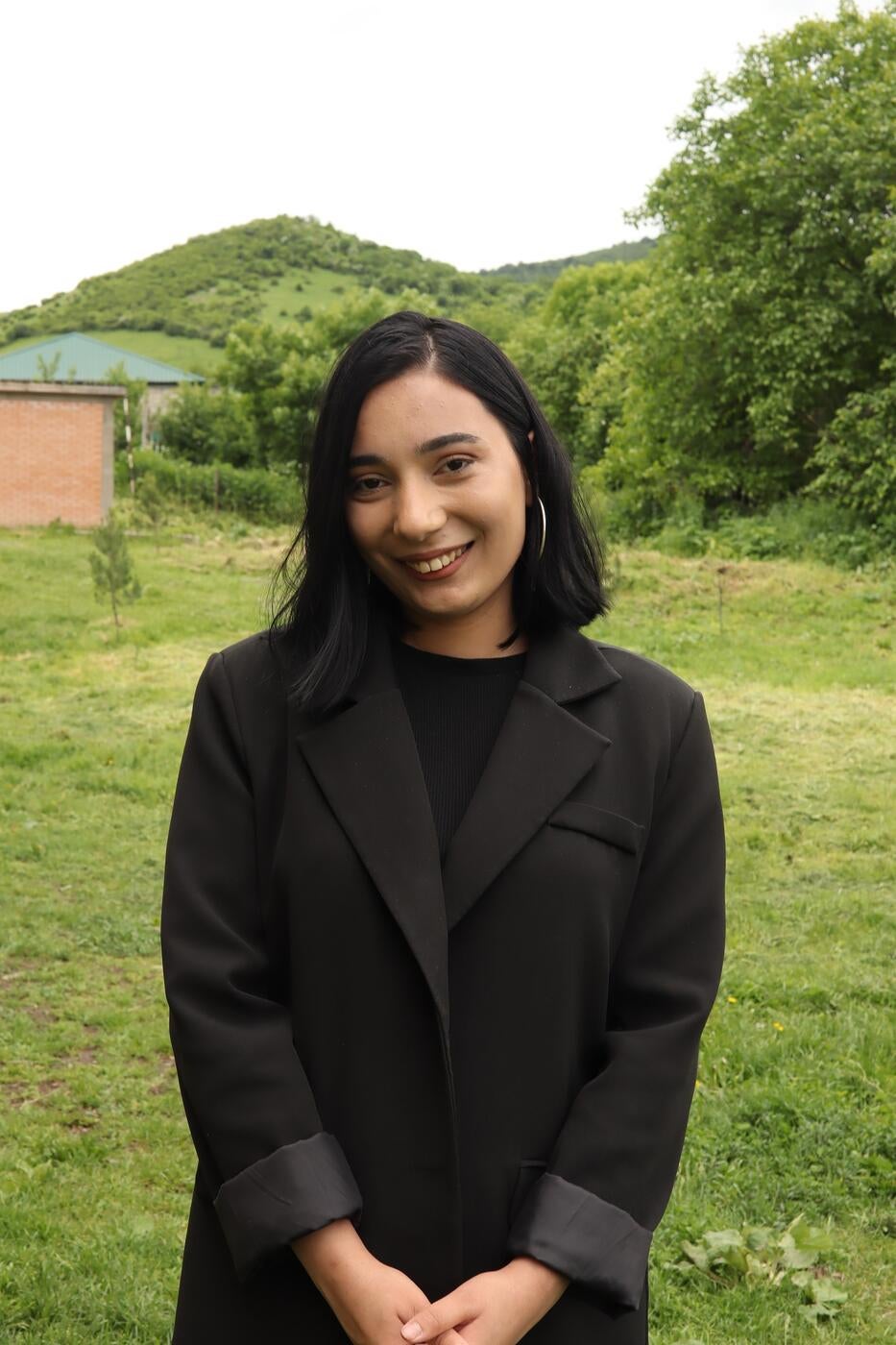 A young woman wearing black is standing in a field, smiling