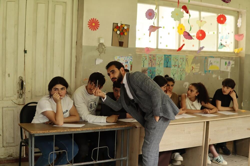 A man is showing something to a bunch of adolescents in a classroom