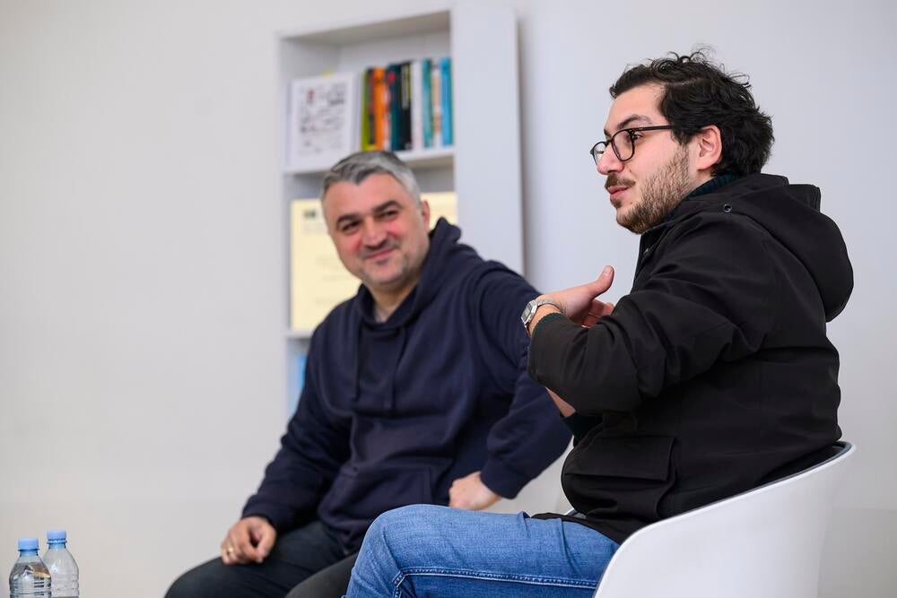 Two men sitting together near a bookshelf