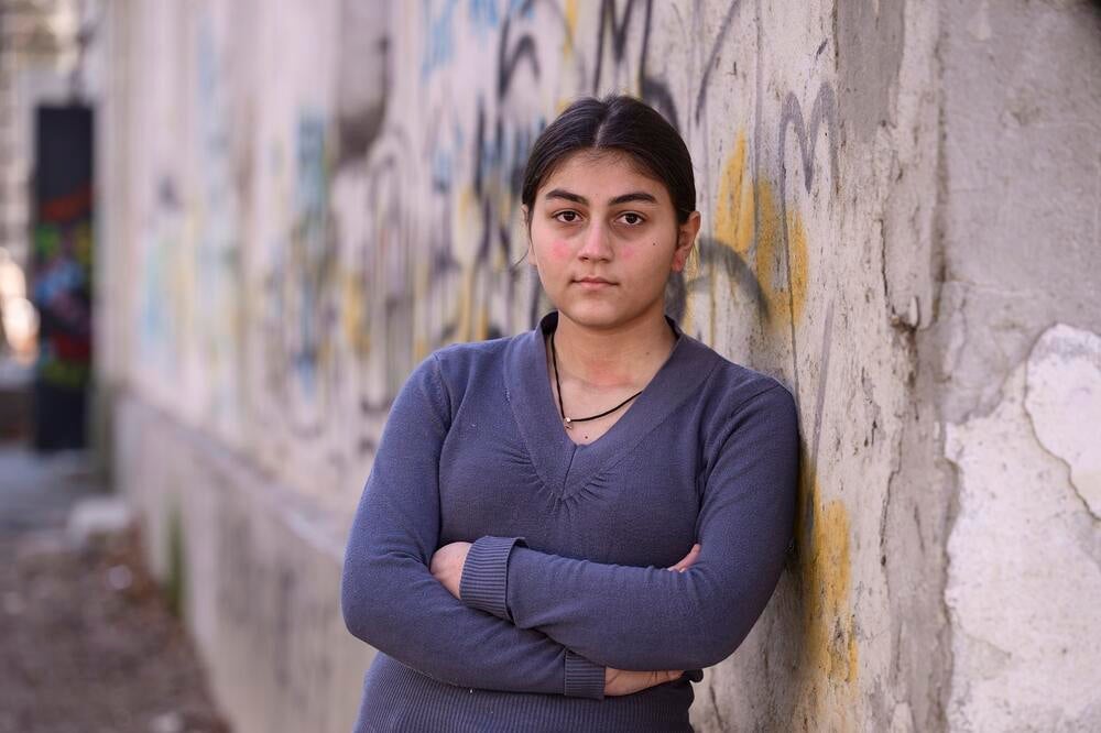 A girl wearing purple shirt is standing at a wall