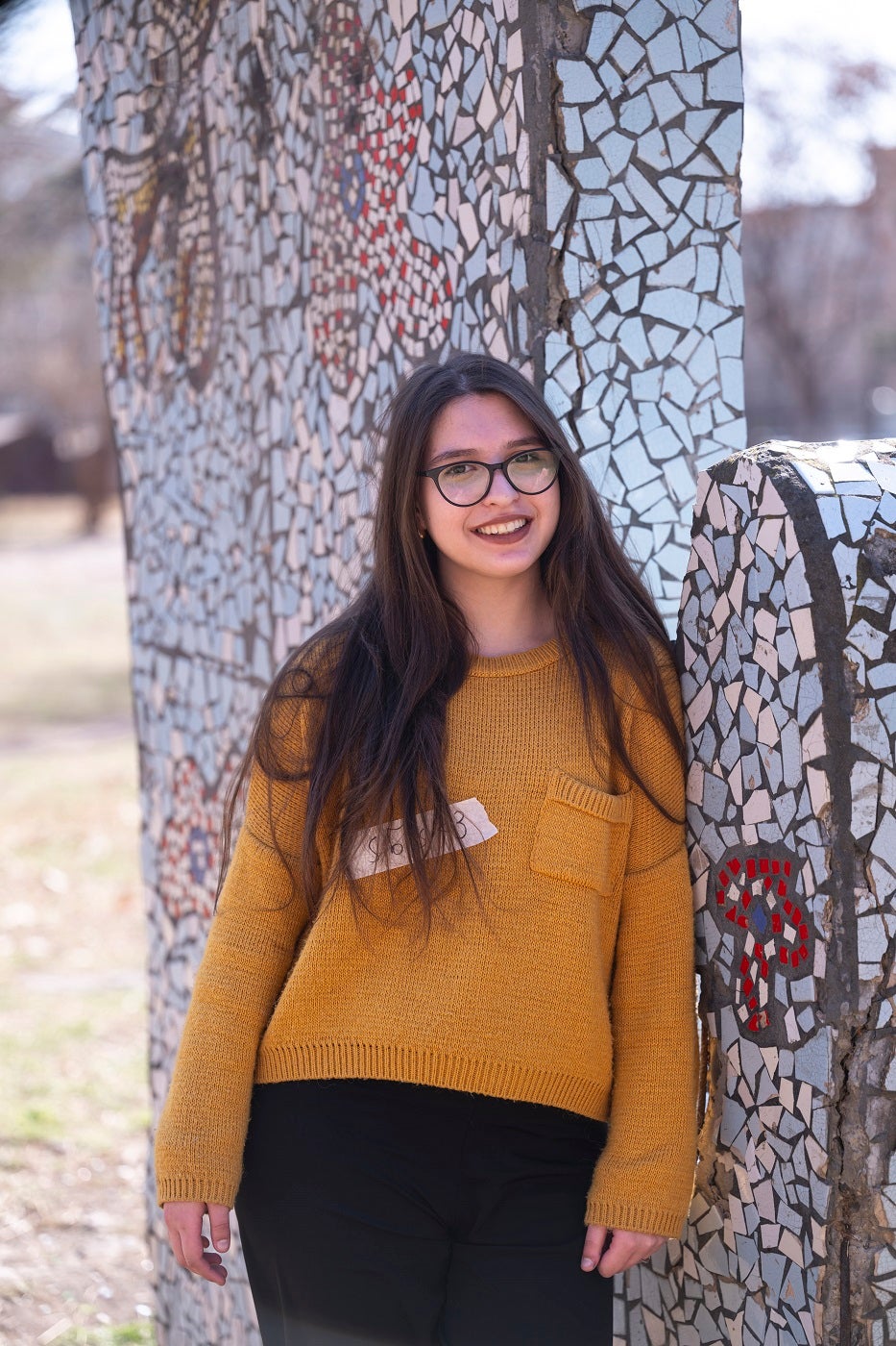 A girl wearing yellow shirt and glasses is standing outdooors