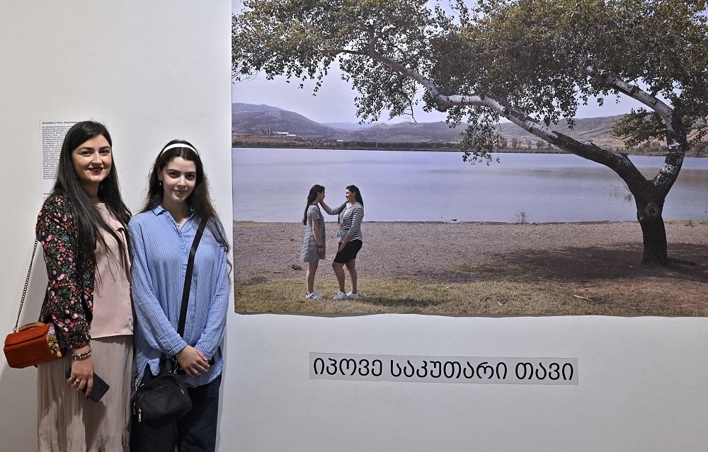 A women and her daughter standing at a wall near their large photo 