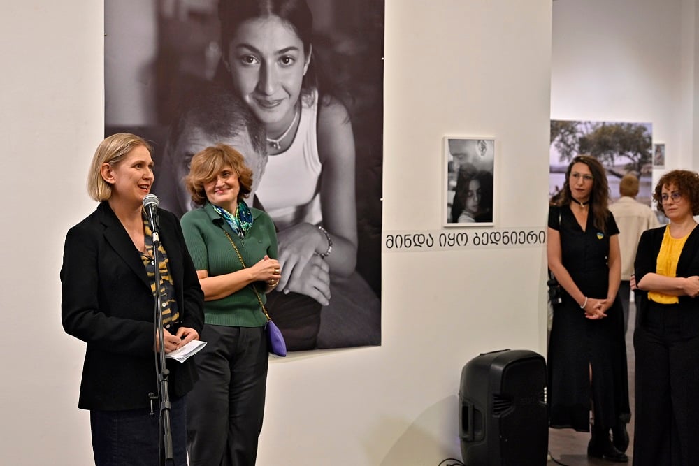 Two women standing at a microphone, while two others are listening