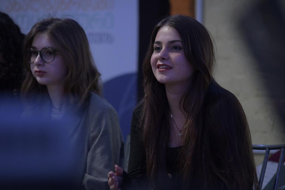 Two young women sitting together, while one of them is talking