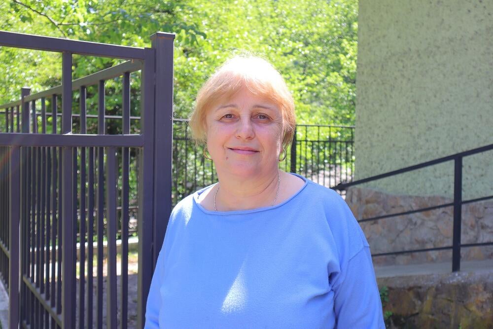 An elder woman wearing blue shirt is standing outdoors
