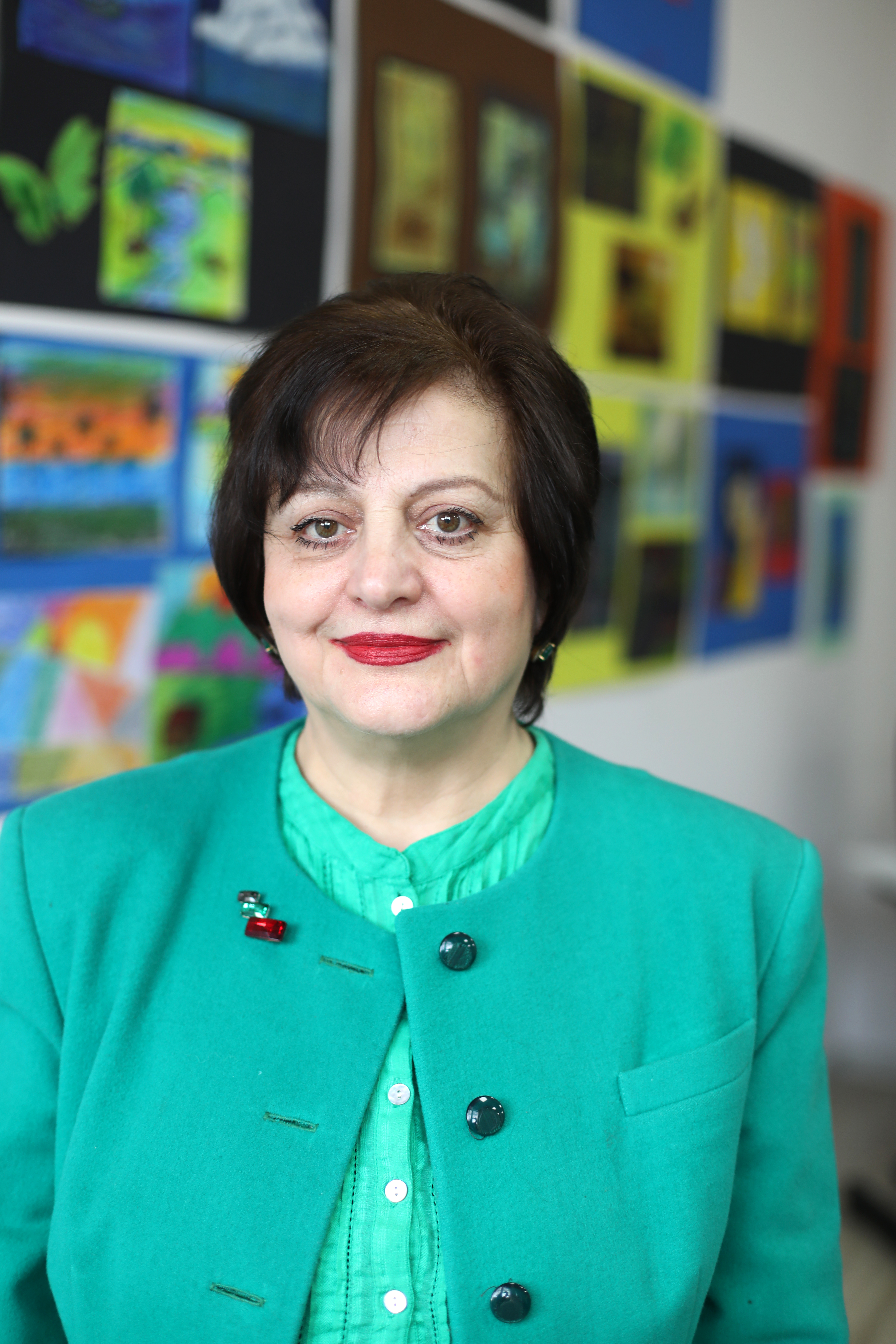 Larisa Sulkhanishvili, wearing a green coat on a green suit, is standing at a wall with paintings