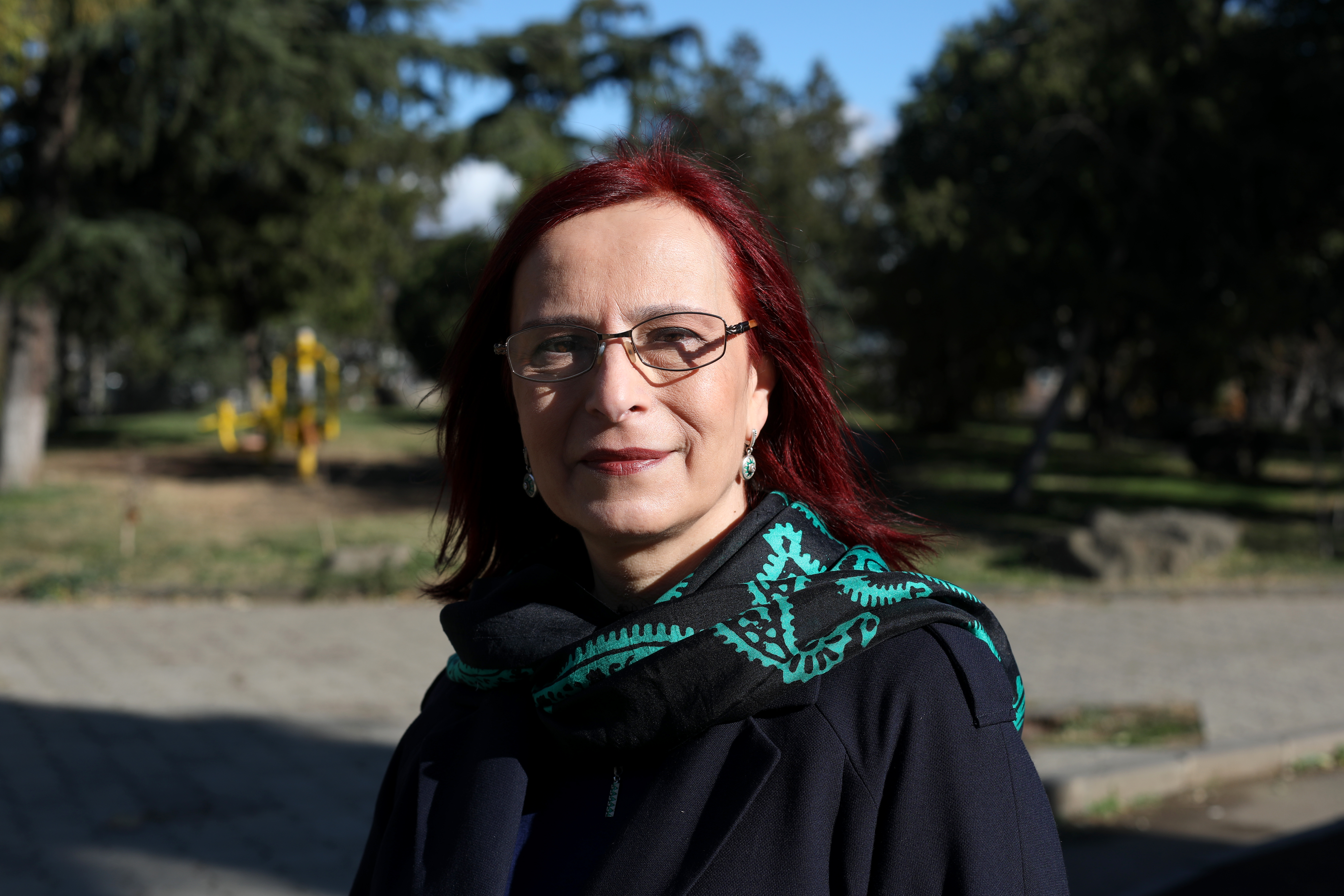 A woman with red hair and glasses standing outdoors
