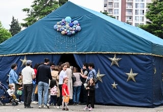 People with kids are standing at a blue tent with yellow start and several balloons