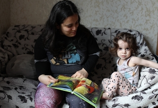 A mom and her daughter sitting on an armchair reading a book