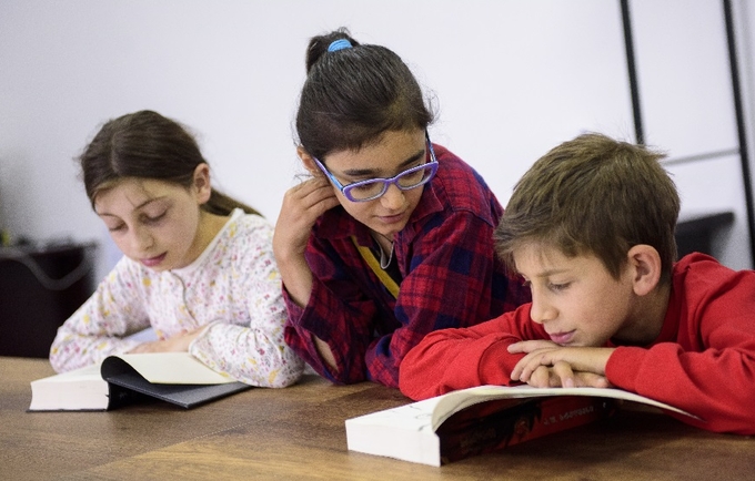 Two girls and a boy sitting together, reading a book