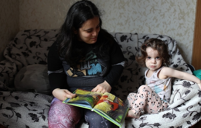A mom and her daughter sitting on an armchair reading a book