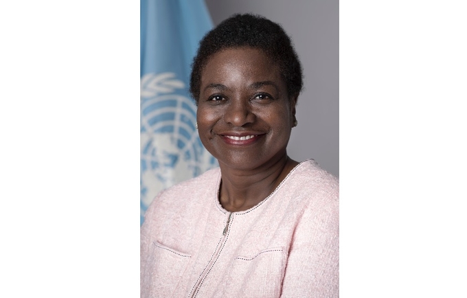 Executive Director of UNFPA Dr. Natalia Kanem, standing in front of UN Flag, wearing pale pink blazer.