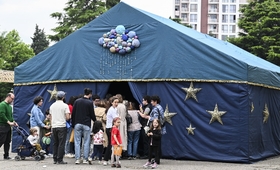 People with kids are standing at a blue tent with yellow start and several balloons