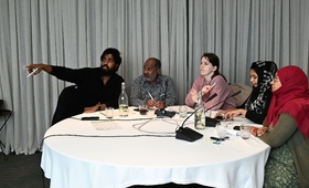 A bunch of people sitting at a roundtable, one of them pointing figure at something