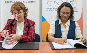 Directors of Hera Clinic and UNFPA Georgia are sitting at a table, signing the memorandums of understanding in front of banners