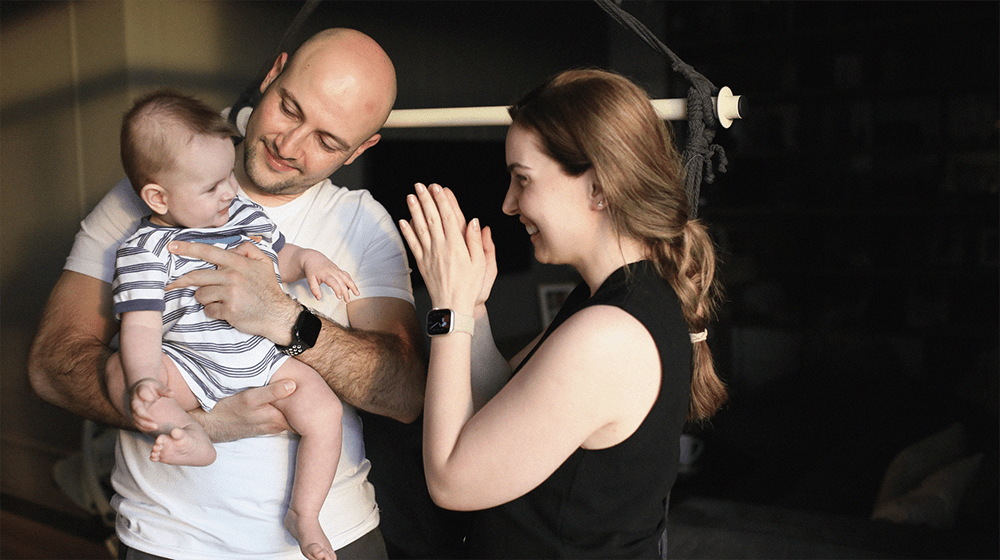 The father holding a baby-boy in his hands, while the mother is clapping hands to make him smile