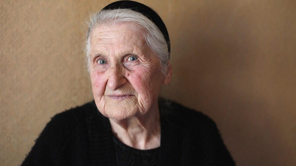 A close up to the face of an elder woman with blue eyes and gray hair