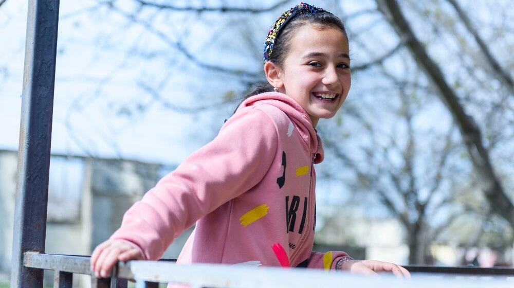 An adolescent girl, standing outdoors, smiling