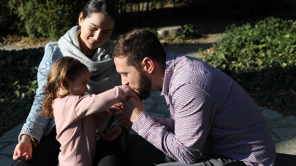 A photo of a mother and a father with their adolescent daughter outdoors 