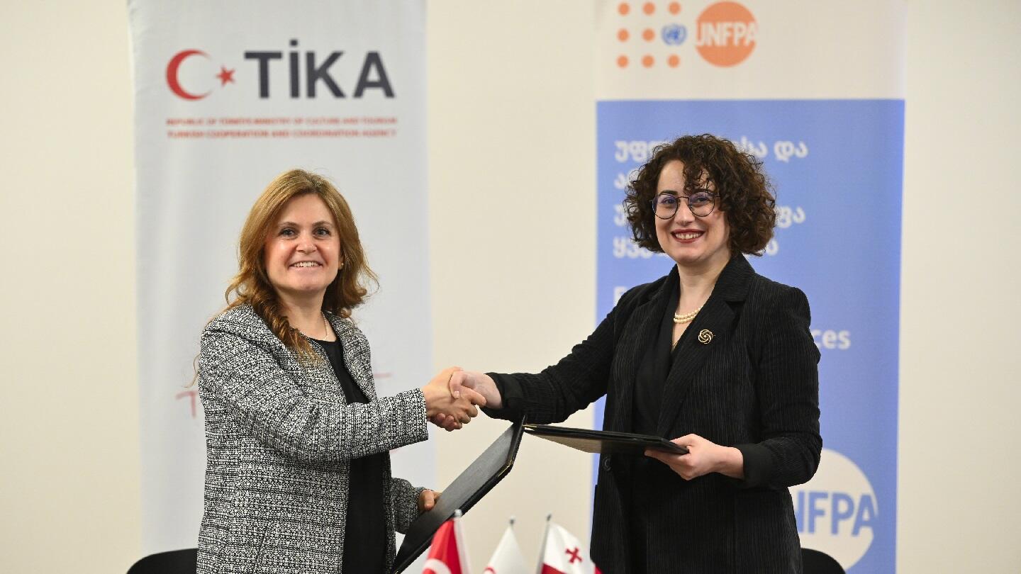 Female representatives of the Turkish Cooperation and Coordination Agency  and the United Nations Population Fund are holding hands