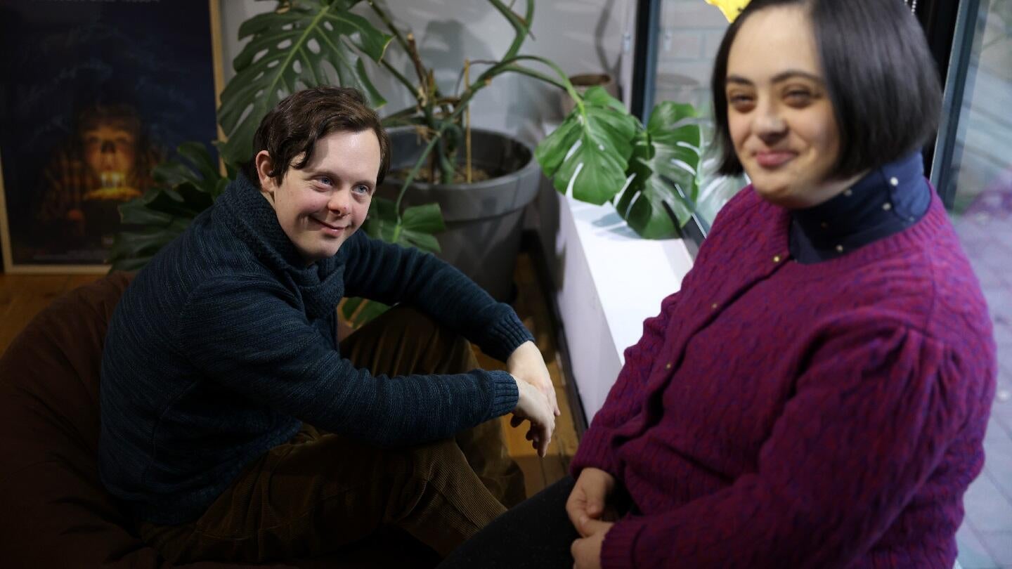 A young man and a boy with down syndrome, standing near a window