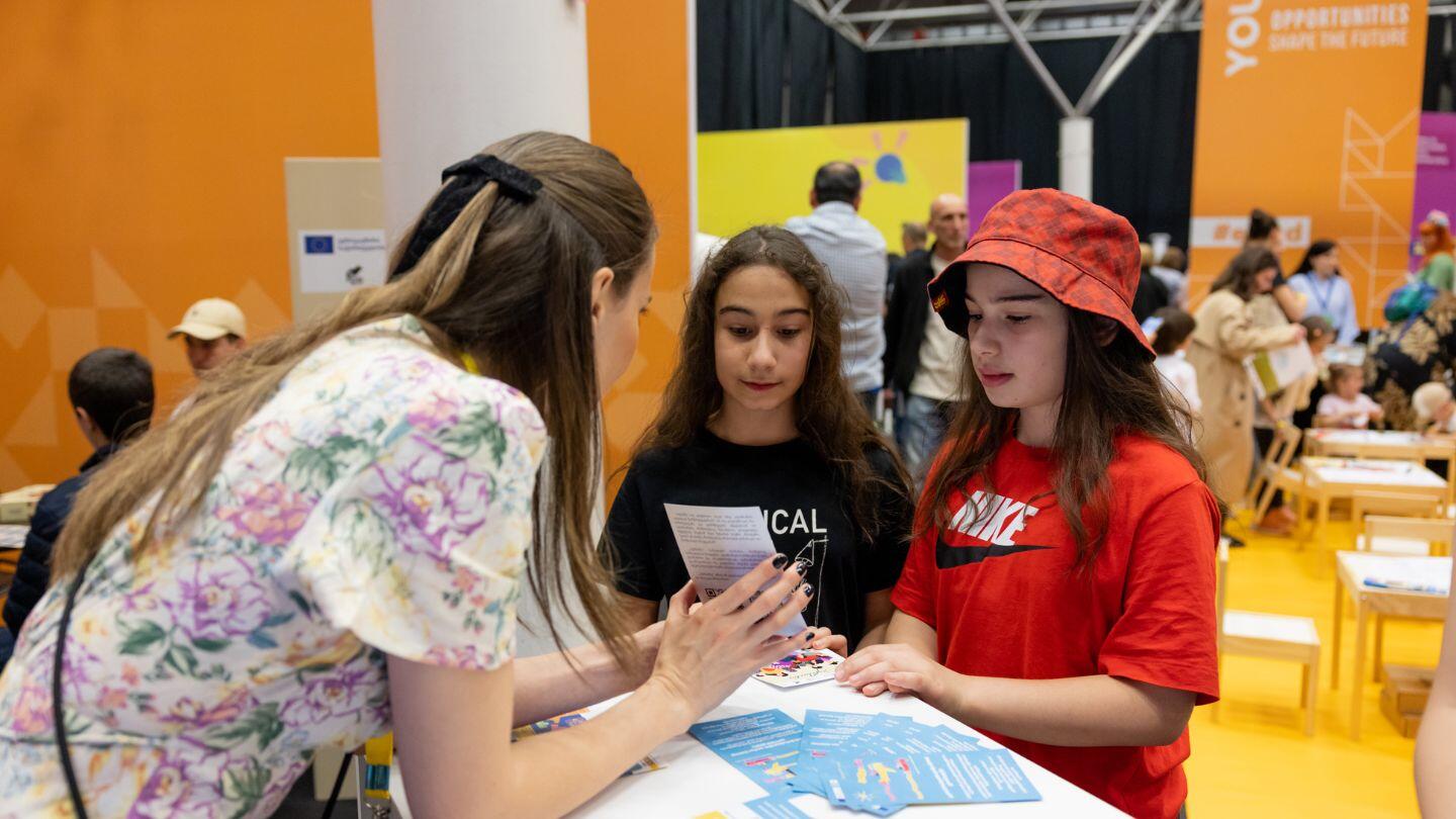 A woman showing two adolescent girls a card