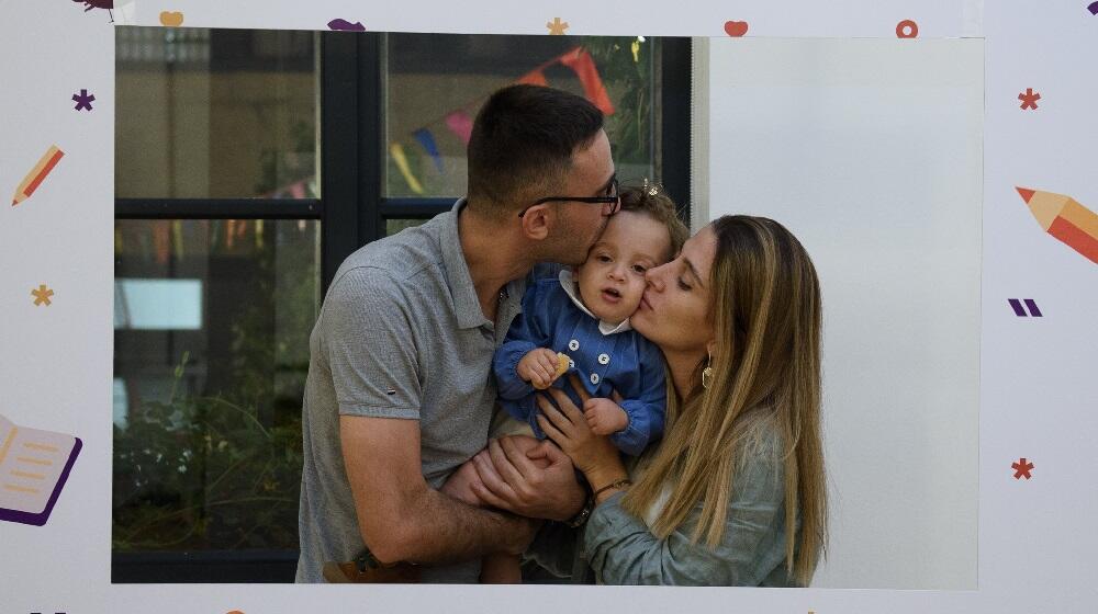 A father and a wife holding their child, kissing