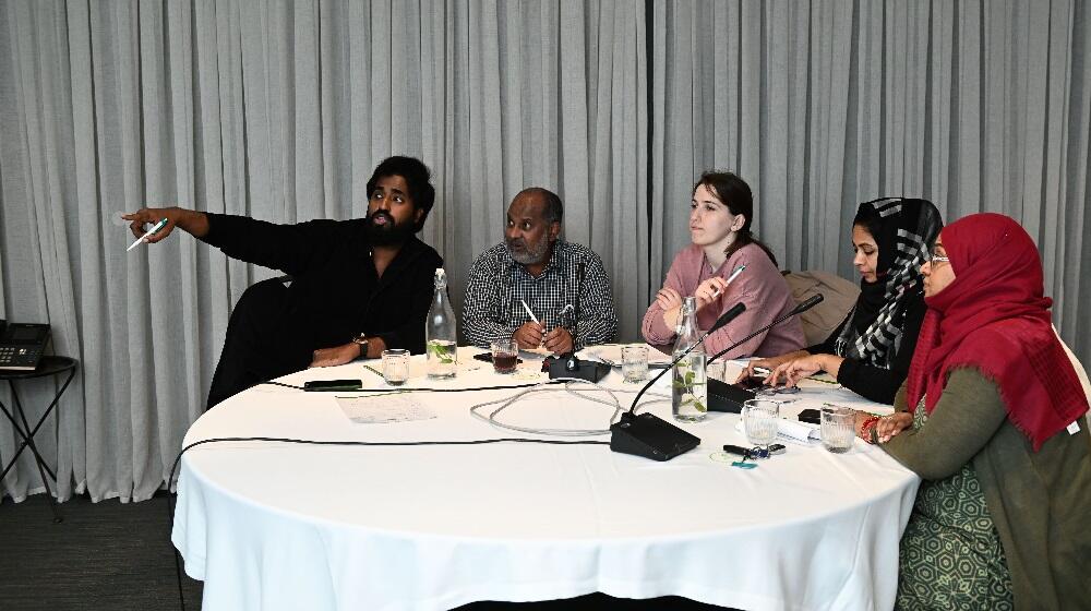 A bunch of people sitting at a roundtable, one of them pointing figure at something