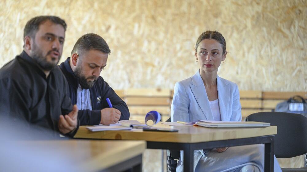 A photo of two men and a woman sitting together. The men are both wearing black, while a women in wearing blue