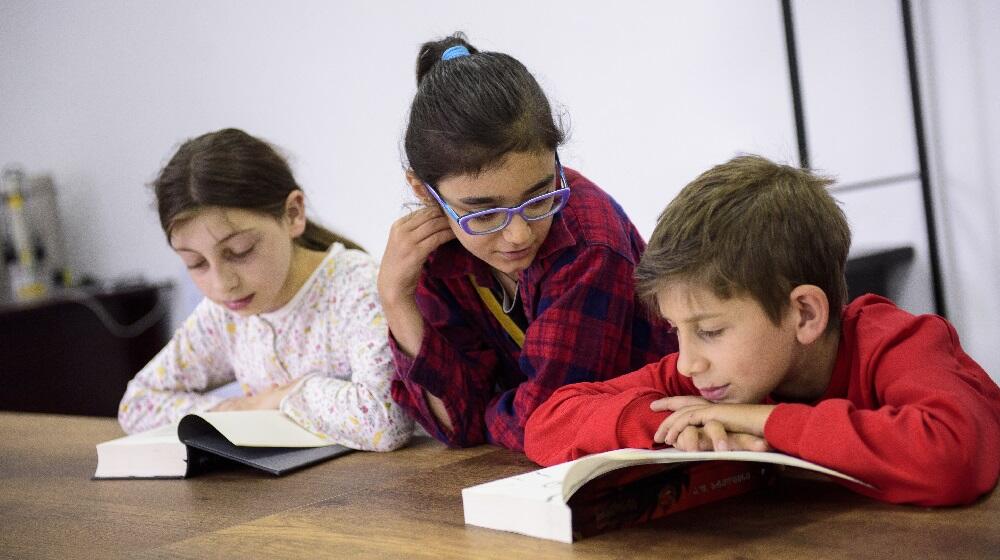 Two girls and a boy sitting together, reading a book