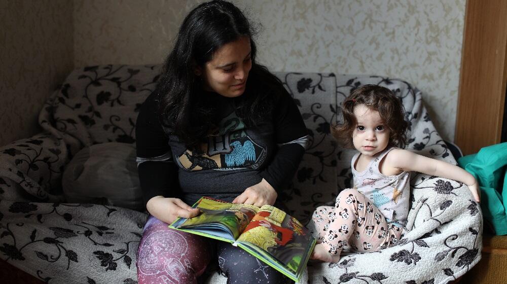 A mom and her daughter sitting on an armchair reading a book