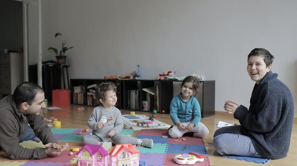 A family of a husband, wife and two children sitting on a carpet