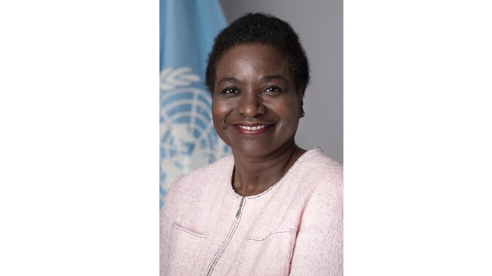 Executive Director of UNFPA Dr. Natalia Kanem, standing in front of UN Flag, wearing pale pink blazer.